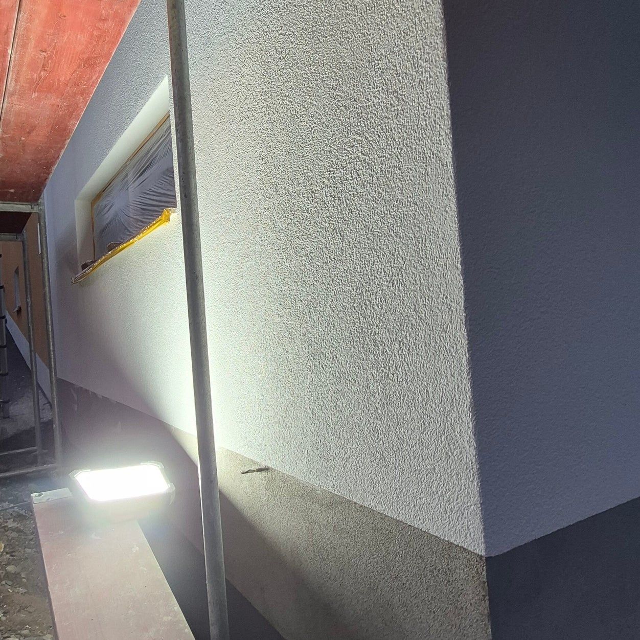 Frisch verputzte Außenwand eines Anbaus mit strukturiertem Putz im Licht eines Baustrahlers